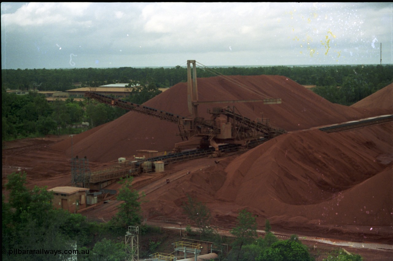 211-03
Weipa, Lorim Point stockpile area viewed from the wharf. A stacker is at the end of the yard belt with the reclaim tunnel for the wharf just visible at the bottom of frame.
