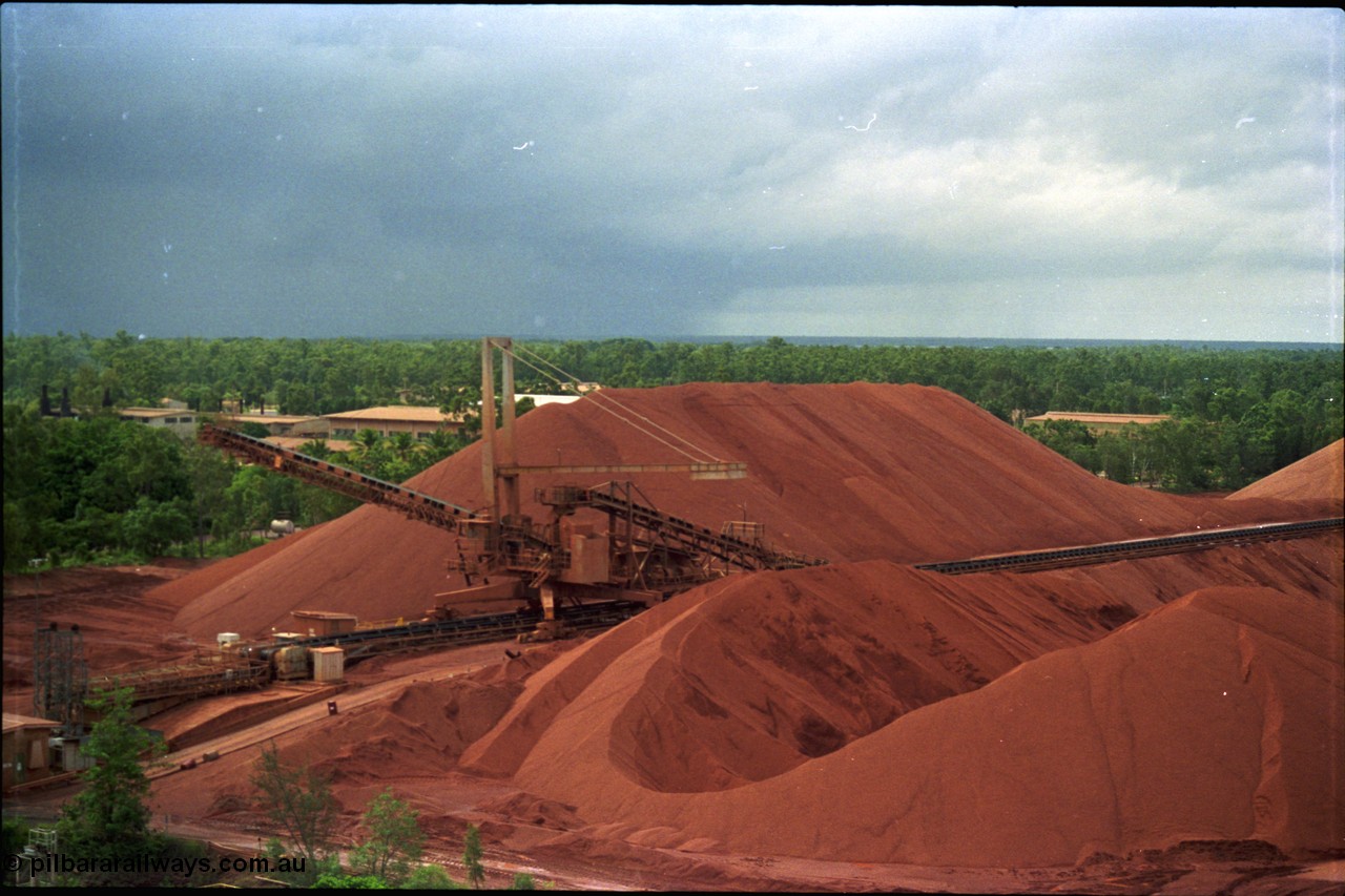 211-09
Weipa, Lorim Point stockpile area viewed from the wharf. A stacker is at the end of the yard belt with the reclaim tunnel for the wharf just visible at the bottom of frame.
