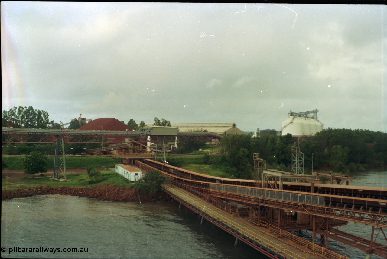 211-34
Weipa, Lorim Point view looking north east from the kaolin loader back towards the bauxite stockpiles, calcination shed and kaolin storage silos. The elevated conveyor is for kaolin, while the two conveyors running under the road to the right are the bauxite loading conveyors.
