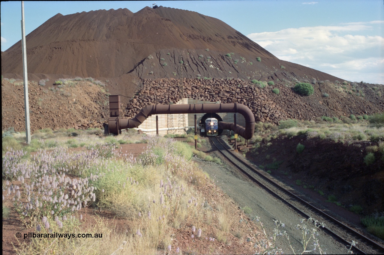 221-21
Yandi One mine loadout balloon loop, General Electric AC6000 class emerges from the loadout portal at 0.9 km/h as it leads a train through the loading vaults, the dust extraction ducting is also visible and the plant stacker can been seen at the very top of the stockpile.
Keywords: GE;AC6000;51062-9;