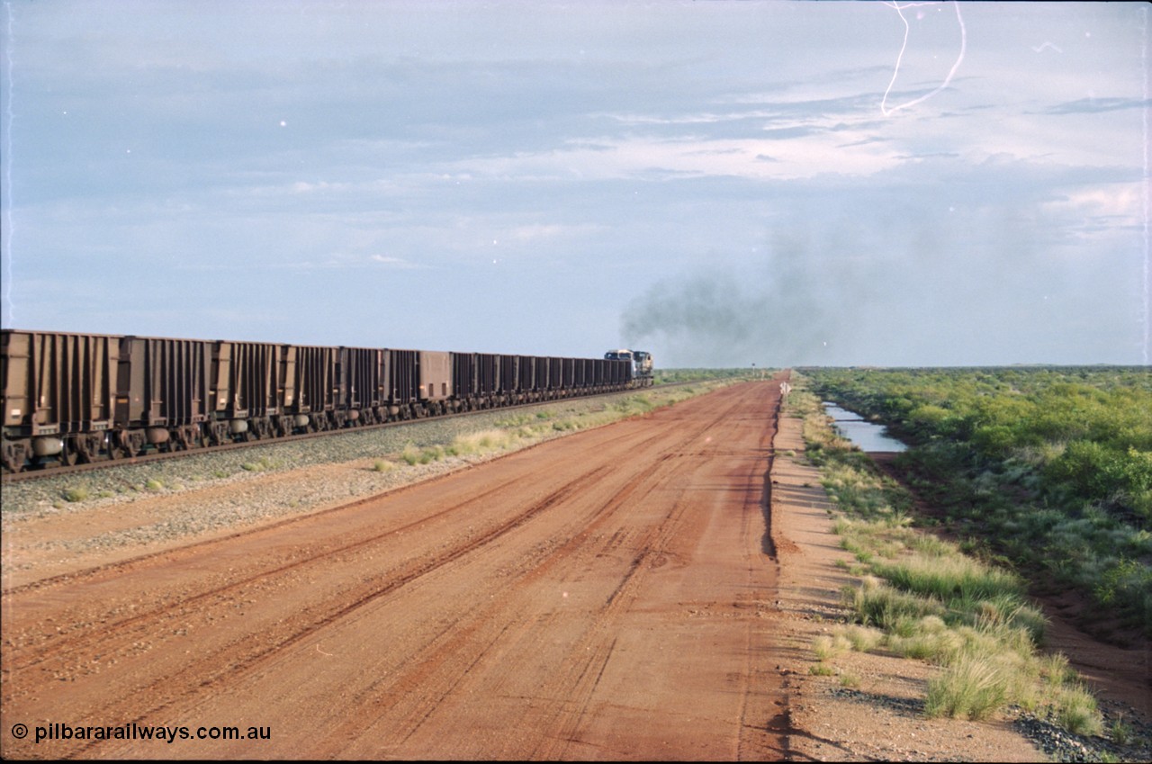 225-23
At the 24.1 km grade crossing on the BHP Newman line, the afternoon departure for Yandi mine heads south behind the standard double General Electric AC6000 units with GE Erie built 6075 serial 51067 second unit to lead sister unit 6074 with another AC6000 unit mid-train. This was before the units were named. [url=https://goo.gl/maps/qGkyfiuy6212]GeoData[/url].
