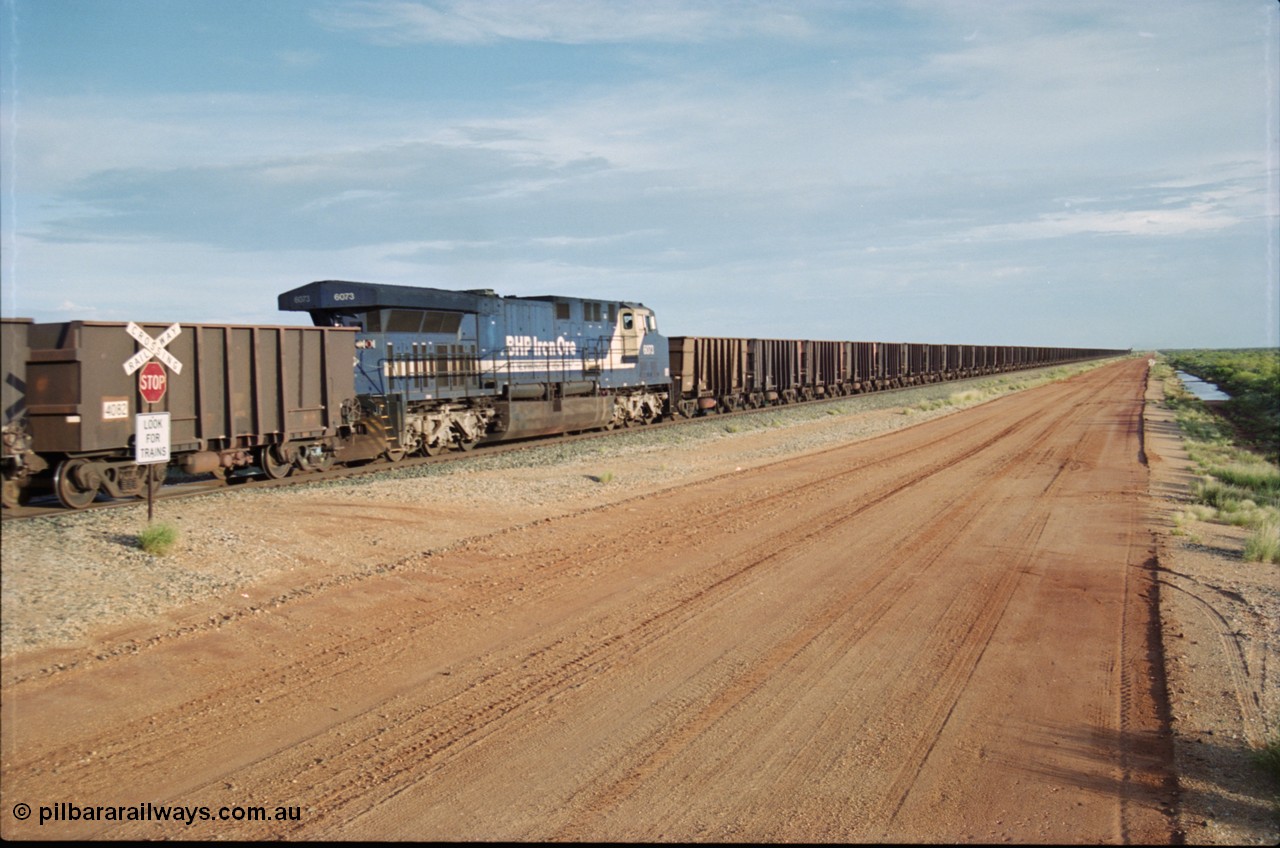 225-24
At the 24.1 km grade crossing on the BHP Newman line, General Electric AC6000 model unit 6073 serial 51065 built at GE Erie is the mid-train remote for the afternoon empty Yandi mine train as it heads south. This was before the units were named. [url=https://goo.gl/maps/qGkyfiuy6212]GeoData[/url].
Keywords: 6073;GE;AC6000;51065;