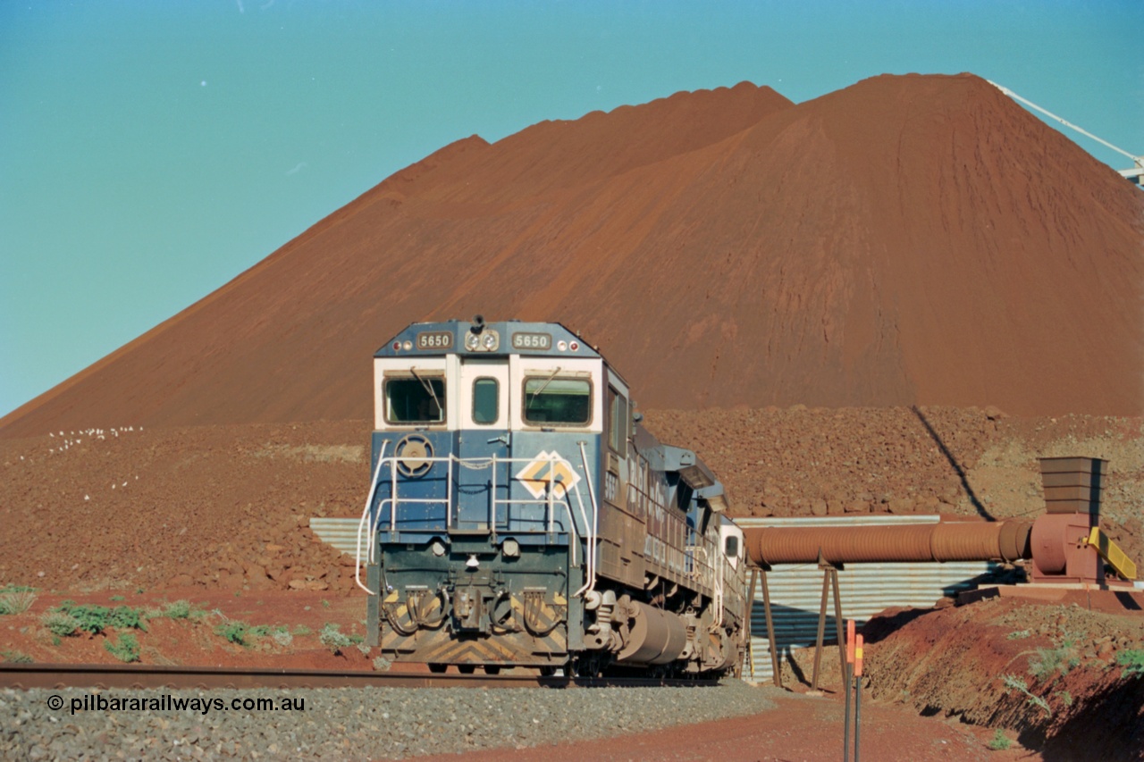 229-20
Yandi Two loadout, looking at the exit portal of the tunnel as Goninan rebuild CM40-8M GE unit 5650 'Yawata' serial 8412-07 / 93-141 drags a loading train through at 1.2 km/h, the massive pile of ore is gravity fed into the waggons via two sets of hydraulic chutes, the original pedestal radial stacker is visible above the ore along with the extraction fan. [url=https://goo.gl/maps/jmtnauf76Zq]GeoData[/url].
Keywords: 5650;Goninan;GE;CM40-8M;8412-07/93-141;rebuild;AE-Goodwin;ALCo;M636C;5481;G6061-2;