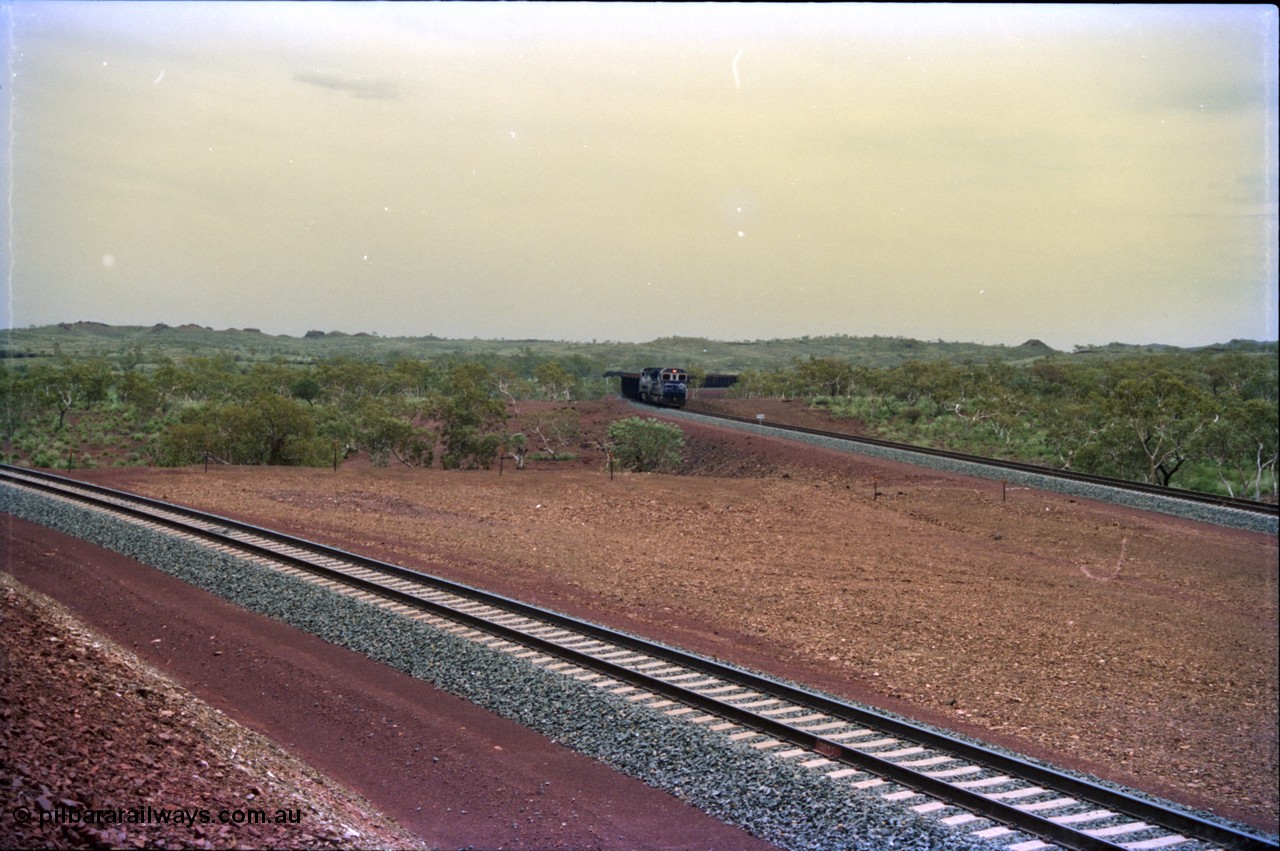 232-04
Yandi Two, view west from near the 311.6 km grade crossing, train can be seen loading on the right. February 1997. [url=https://goo.gl/maps/3tst5WV949N2]GeoData[/url].
