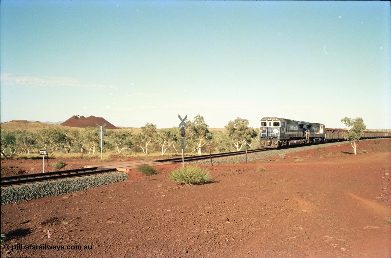 234-32
Yandi Two, BHP Iron Ore Goninan rebuild CM40-8M GE unit 5658 'Kakogawa' serial 8412-03 / 94-149 on the front of a 240 waggon loaded train, this configuration was trialled for a time with two Dash 8 locos, 120 waggons, Dash 8, 120 waggons and Dash 8. View looking across the YT315.8 km grade crossing and 5658 back to the ore stockpile at the loadout. Circa 1998.
Keywords: 5658;Goninan;GE;CM40-8M;8412-03/94-149;rebuild;AE-Goodwin;ALCo;M636C;5480;G6061-1;