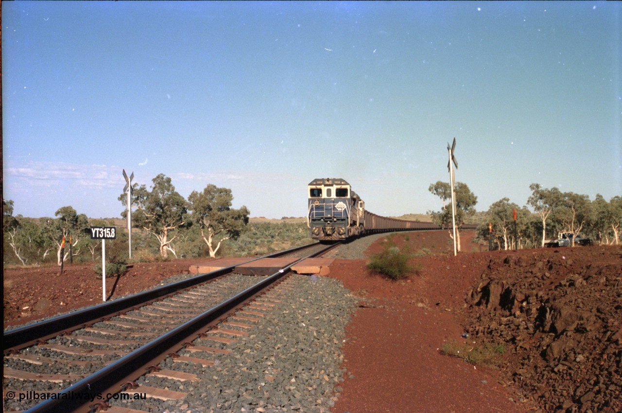 234-34
Yandi Two, BHP Iron Ore Goninan rebuild CM40-8M GE unit 5658 'Kakogawa' serial 8412-03 / 94-149 on the front of a 240 waggon loaded train, this configuration was trialled for a time with two Dash 8 locos, 120 waggons, Dash 8, 120 waggons and Dash 8. View looking across the YT315.8 km grade crossing and 5658 back to the ore stockpile at the loadout. Circa 1998.
Keywords: 5658;Goninan;GE;CM40-8M;8412-03/94-149;rebuild;AE-Goodwin;ALCo;M636C;5480;G6061-1;