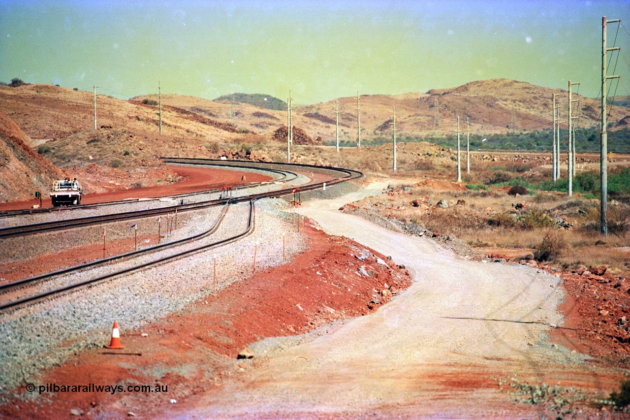 246-04
Cape Lambert, yard view of the then new extension to the south for the West Angelas mine was coming on stream, the just visible siding (rejoining) on the far left will become a compressor waggon holding road, the 6 km and Boat Beach Rd grade crossing are around the corner to the left. Closest to the camera is the extended No. 1 Road which becomes the Empty Car Line from car dumper one for the Deepdale traffic. Next is the original line or Mainline and the third line across is the Loaded Car Line for the West Angelas traffic to the new car dumper 2. The Boat Beach Rd can be seen on the extreme right. 22nd May 2002.
