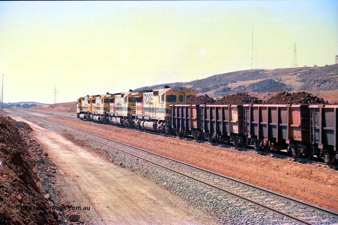 246-27
Cape Lambert, a Robe River loaded Deepdale train rolls along the mainline behind the standard quad Dash 8 power with 202 waggons with newly extended roads either side of it. In the distance can be seen are the railway workshops. 22nd May 2002.
