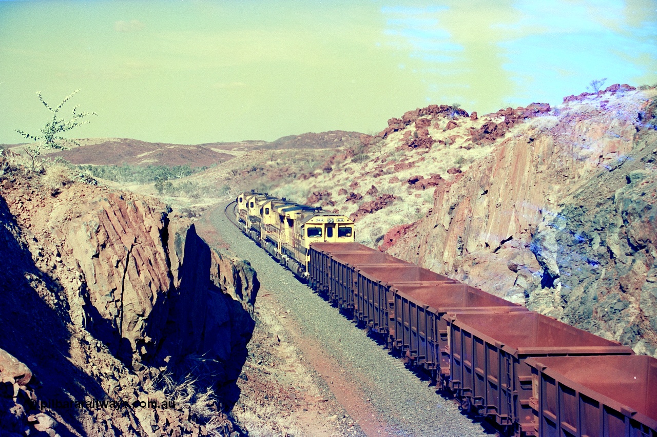 247-35
Near Cooya Pooya at the 37.5 km on the Robe River Cape Lambert line an empty train passes under the town water supply pipeline and pass through Lockyer Gap behind the standard Robe power of quad CM40-8M or Dash 8 locomotives led by 9425 with 9410, 9420 and last unit 9414 which is a Goninan WA ALCo to GE rebuild CM40-8M with serial 8206-11 / 91-124 from November 1991 riding on Dofasco bogies and was originally an AE Goodwin built M636 ALCo built new for Robe in December 1971 and numbered 262.005, later numbered 1714. Location is [url=https://goo.gl/maps/nLyndU6bg2HA5SZX6]here[/url].22nd May 2002.
