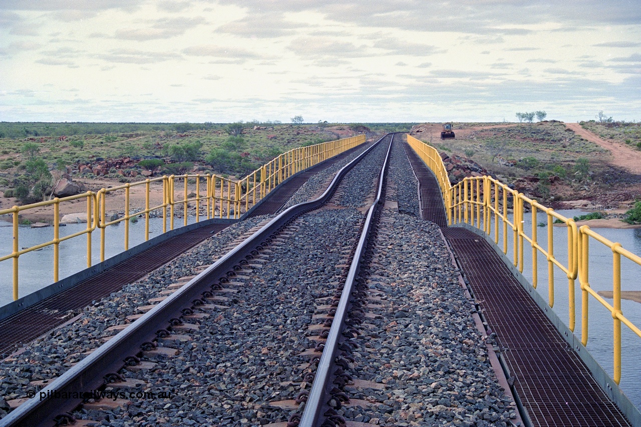 249-04
Yule River bridge looking north from the 160 km on the BHP mainline. The third pier from the southern end was undermined by flood waters from Tropical Cyclone John in December 1999. The rail line was closed for two weeks while repairs were effected. Approximate [url=https://goo.gl/maps/phCWr8u1xnuBdzwj6]location[/url].
