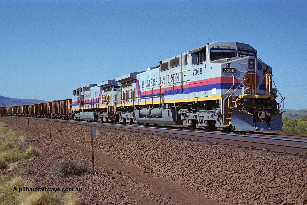 250-03
Pelican Siding on the Hamersley Iron Tom Price line about the 208 km with an empty train behind the standard pairing of two General Electric built 9-44CW units 7068 serial 47747 and 7067 serial 47746 stand on the loop or passing track for a meet with a loaded train. 21st October 2000.
Keywords: 7068;GE;Dash-9-44CW;47747;