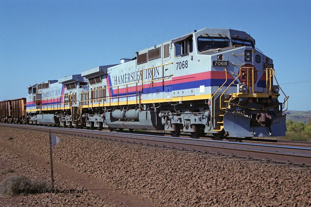 250-04
Pelican Siding on the Hamersley Iron Tom Price line about the 208 km with an empty train behind the standard pairing of two General Electric built 9-44CW units 7068 serial 47747 and 7067 serial 47746 stand on the loop or passing track for a meet with a loaded train. 21st October 2000.
Keywords: 7068;GE;Dash-9-44CW;47747;