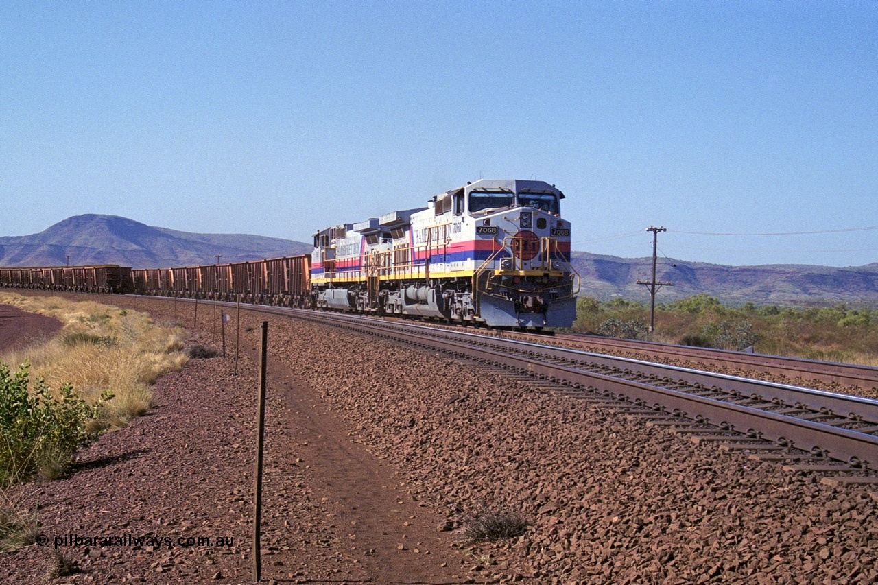 250-14
Pelican Siding on the Hamersley Iron Tom Price line about the 208 km with an empty train behind the standard pairing of two General Electric built 9-44CW units 7068 serial 47747 and 7067 serial 47746 stand on the loop or passing track for a meet with a loaded train. 1550 hrs 21st October 2000.
Keywords: 7068;GE;Dash-9-44CW;47747;
