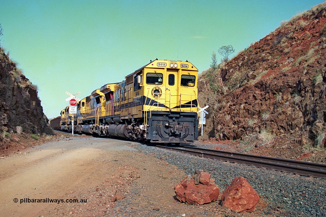 256-33
At the 89.6 km grade crossing the loaded train behind the quad CM40-8M working of 9414, 9420, 9410 and 9425 rolls across the crossing and heads down the 1.26 percent grade. 9414 was built by AE Goodwin NSW as an ALCo M636 model in December 1971 with serial number G-6060-5 and part of the original order for five units. Locomotive was delivered to Robe River in January 1972 with Bechtel Pacific road umber 262.005 for construction use and was renumbered 1714 when that was completed. 9414 was rebuilt by Goninan WA in November 1991 to become an CM40-8M model with serial number 8206-11 / 91-124. May 2002.
Keywords: 9414;Goninan;GE;CM40-8M;8206-11/91-124;rebuild;AE-Goodwin;ALCo;M636;G6060-5;