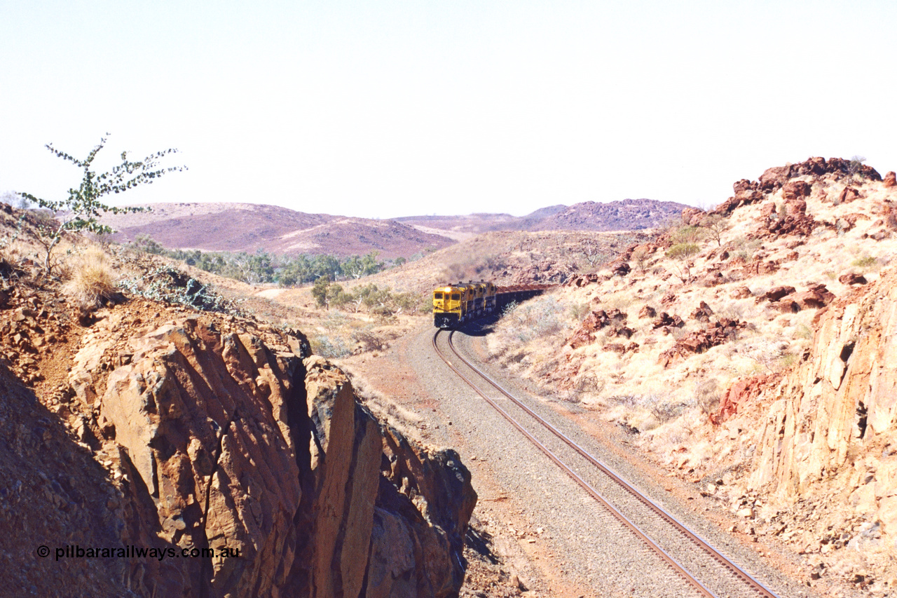 283-29
Near Woodbrook as the train rounds the curve just north of the 38.5 km grade crossing and through the cutting that will see it pass under the water pipe bridge behind the quad Robe River CM40-8M working of 9414, 9420, 9410 and 9525 with 202 waggons bound for Cape Lambert. 22nd of May 2002.

