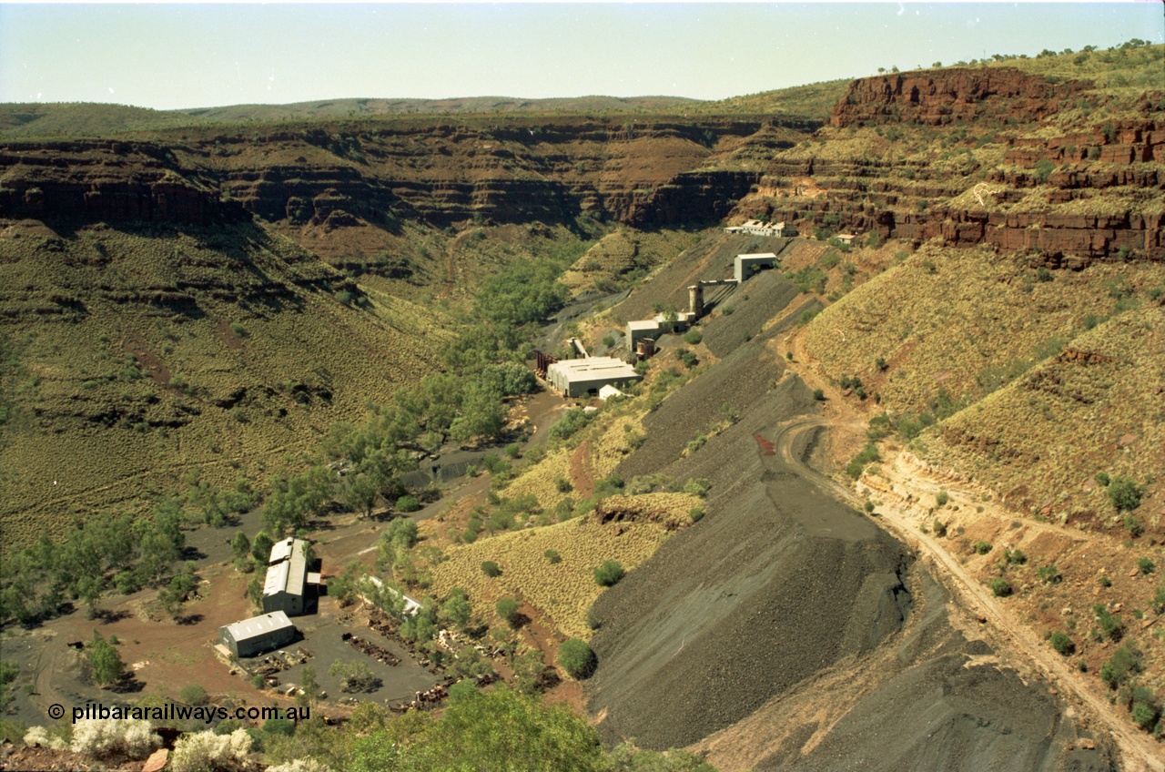195-15
Wittenoom, view from the Devil's Staircase of Colonial Mill and Mine with piles of tailings, the building and yard at the bottom of the frame is the warehouse or store and gated yard with the workshop being the larger of the two, the buildings at the top level are the locomotive and underground mining offices and workshops, with the crusher and milling and bagging plant using gravity to its advantage.
