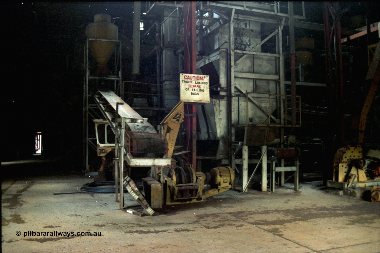 195-24
Wittenoom Gorge, Australian Blue Asbestos or ABA Colonial Mill, view inside part of the bagging plant within the mill, near the truck loading area, JCB backhoe can be seen behind conveyor.
