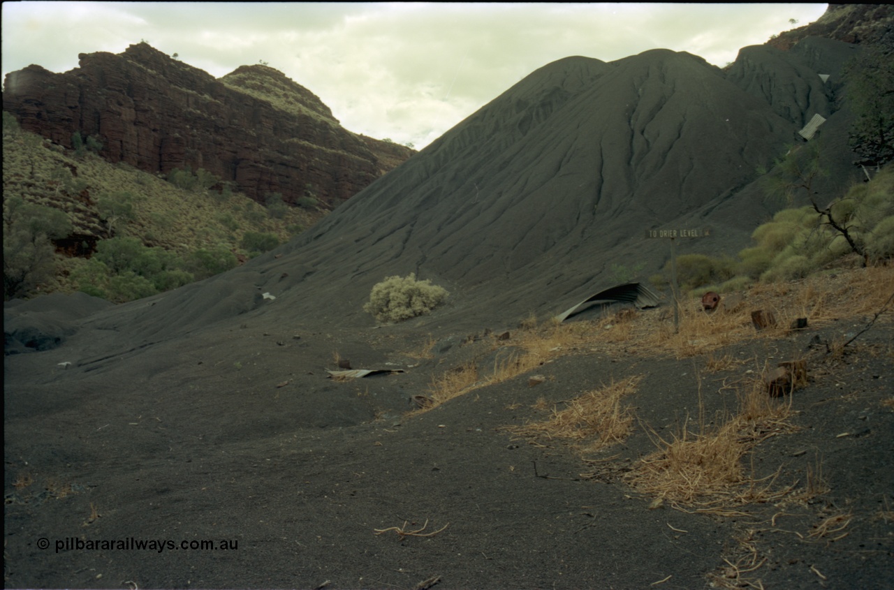 195-28
Wittenoom Gorge, Australian Blue Asbestos or ABA Colonial Mill, view of tailings which weather has eroded over the roads, direction sign to Drier Level still visible.
