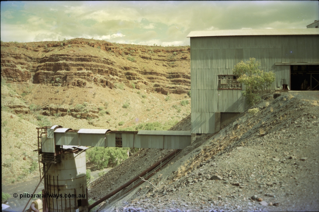 195-36
Wittenoom Gorge, Australian Blue Asbestos or ABA Colonial Mill, view of primary crushing building, shows conveyor housing and silo structure with piping and a steep stair walkway from the lower levels to the crushing shed.
