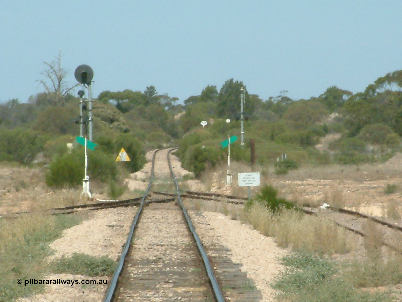 030405 140102
Kyancutta, yard view looking south along the narrow gauge mainline with the siding point levers and indicators with the Eyre Highway grade crossing and one of only three electrically lit signals on the Eyre Peninsula Division. The cast iron 'Yard Limit' sign can be made out in the distance, 5th April 2003.
