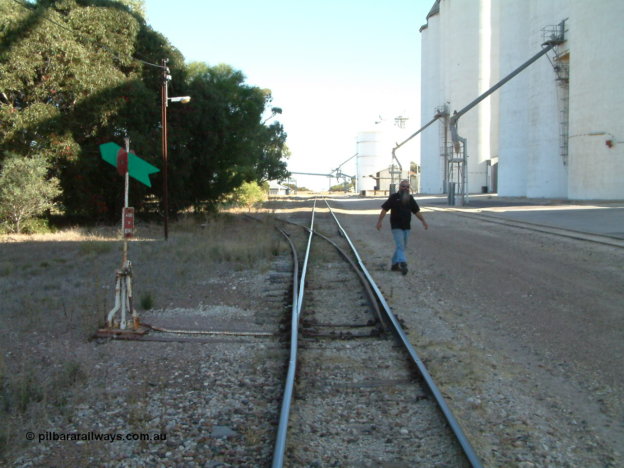 030405 155300
Lock, yard overview looking south, points and lever with indicator for the siding off the mainline, concrete silo complex Block 2 and outflow spout visible on the right as local identity Pope Searle wanders around the yard. 5th April 2003.
