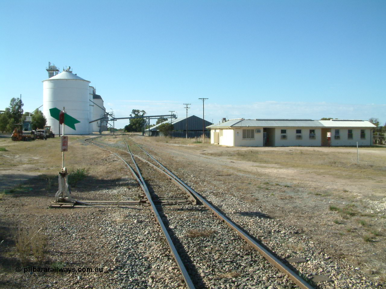 030405 160328
Lock, station yard overview, located at the 148.5 km, originally opened in May 1913 and called Terre after a local property, renamed to Lock in December 1921. Looking north along the mainline, points, lever and indicator for grain siding, Ascom style silo complex with concrete behind them, horizontal grain shed on the right with former crew barracks in front of that. 5th April 2003.
