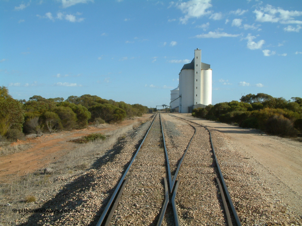 030406 082752
Murdinga, yard overview looking north from the south end with the grain loop branching off on the right, concrete silo complex with horizontal grain shed and Ascom style steel silo complexes with outflow spout and gantry visible. 6th April 2003
