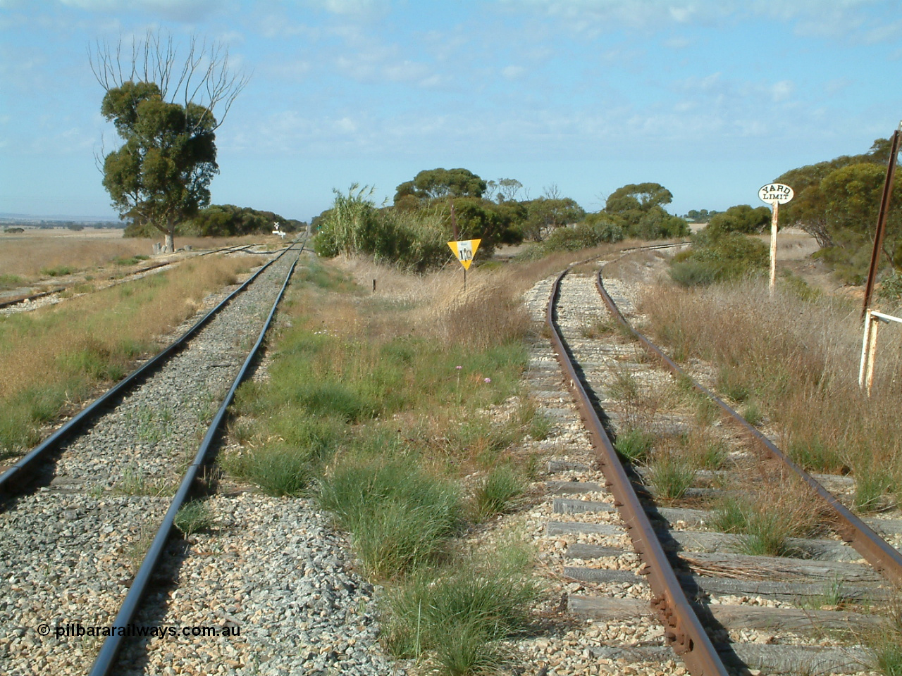 030406 092831
Yeelanna, yard view looking south, shows mainline and grain siding running south and branch line to Kapinnie and former Mount Hope branch curving away to the right across a culvert and past a cast Yard Limit sign. 6th April 2003.
