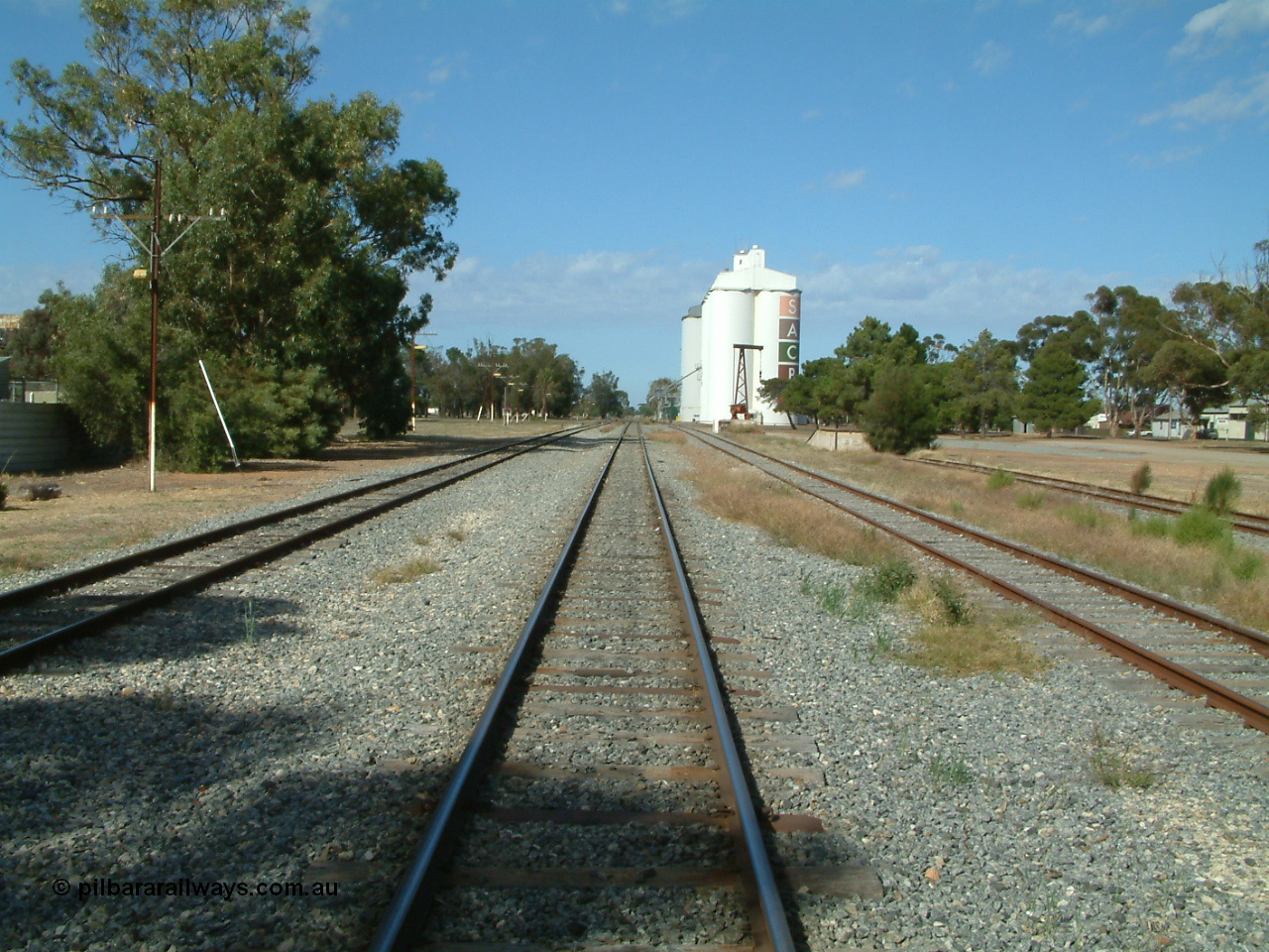 030406 094232
Cummins, yard overview looking south down the mainline through the middle of the yard. Buckleboo line on the left, with the grain and loading ramp sidings on the right. Loading ramp, rotating crane and concrete silos complexes visible in the background. 6th April 2003.
