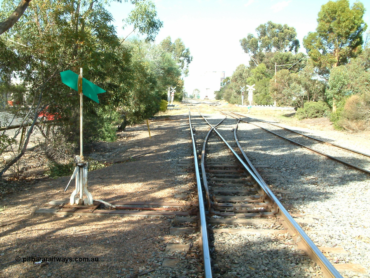 030406 094830
Cummins, yard overview looking south down the Buckleboo line with the mainline from Thevenard on the right, with points, levers and indicators for the crossover and then the grade crossing on Hall St being visible, concrete silos in the distance. 6th April 2003.
