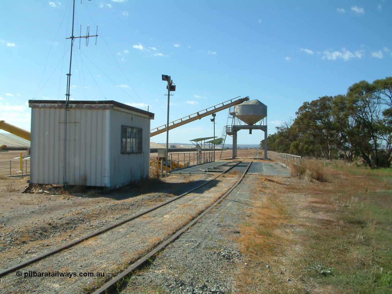 030406 101028
Cummins, view looking from Cummins of the grain bunker rail unloading facility with dual DOH 'Drive Over Hopper' and stackers for loading road vehicles and with the original overhead outflow bin and feed conveyor for loading rail waggons. Loaded bunkers visible on the left. 6th April 2003.
