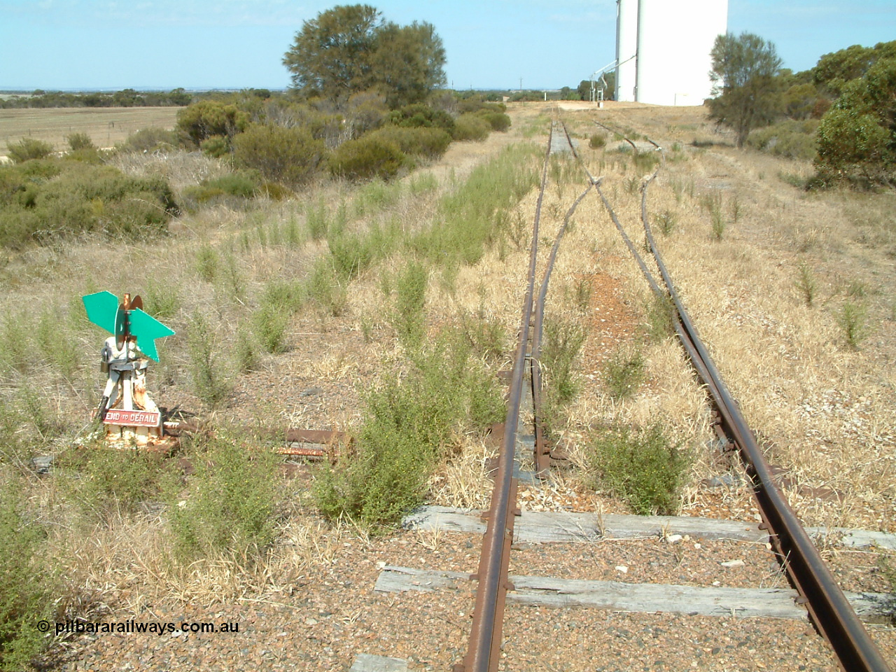 030406 141824
Kapinnie, station yard overview looking east towards Yeelanna, from the terminus end of line with dwarf point lever and indicator, concrete silo complexes with outflow spouts, scotch block visible on siding. 6th April 2003.
