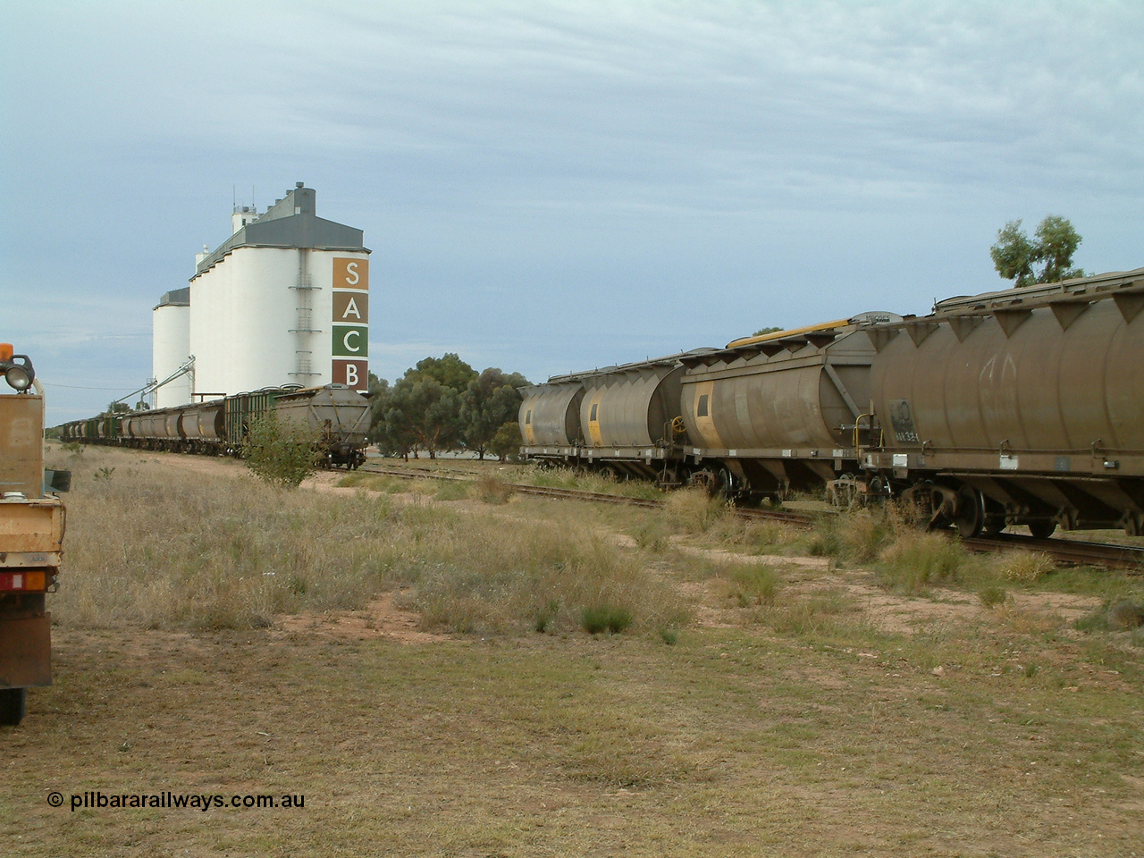 030407 082655
Wudinna, view looking south as the empty rake of bogie grain waggons is shunted into the siding for loading, showing HAN and HCN types of bogie grain hoppers. Concrete SACBH grain complex. 7th April 2003.
Keywords: HAN-type;HCN-type;SAR-Islington-WS;Tulloch-Ltd-NSW;