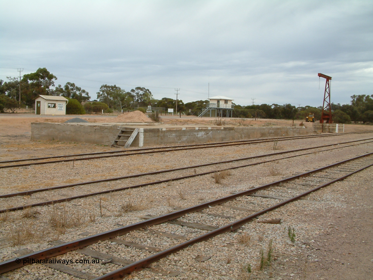 030407 094425
Minnipa, yard view of loading ramp and former site of goods shed, rotating jib crane and road vehicle weighbridge scale room and grain truck sampling building in the background. 7th April, 2003.
