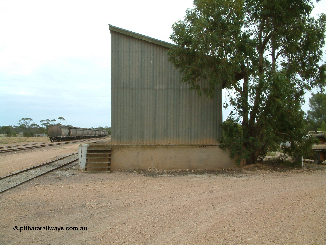 030407 104921
Poochera, south elevation of goods shed and platform, loaded rake of grain waggons awaits pick in the background. 7th April 2003.
