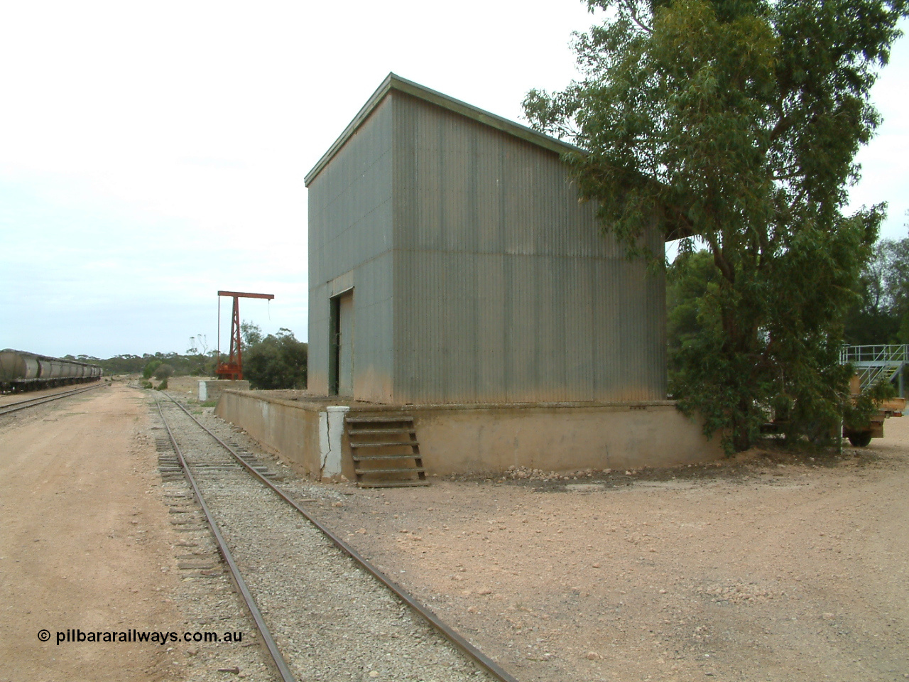 030407 104934
Poochera, south western elevation of goods shed and platform with rotating jib crane in the distance, loaded rake of grain waggons awaits pickup to the left. 7th April 2003.
