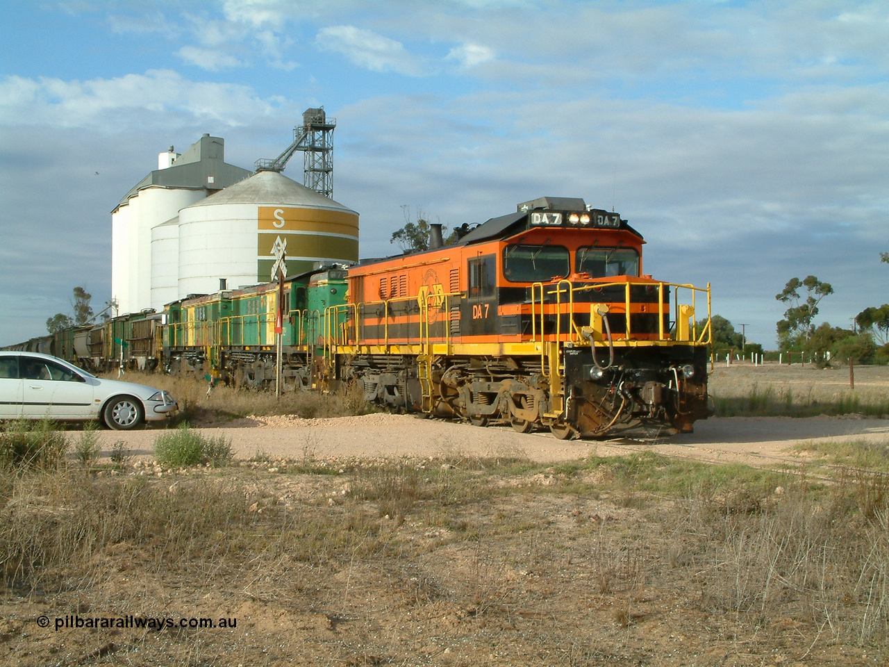 030409 080717
Warramboo, empty grain prepares to get underway following a crew change. Rebuild unit DA 7 in Australian Southern orange and black livery leads a pair of AE Goodwin built ALCo model DL531 830 class units 872 and 871, the relieved crew get in their car with the SACBH concrete silo complex behind.
Keywords: DA-class;DA7;83713;Port-Augusta-WS;ALCo;DL531G/1;48-class;4813;rebuild;