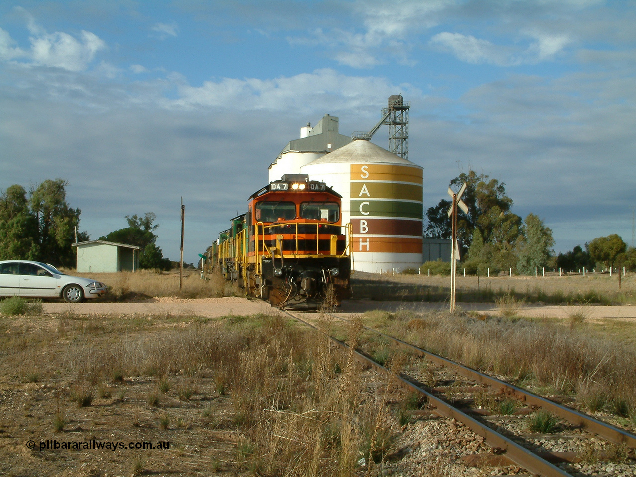030409 080811
Warramboo, empty grain prepares to get underway following a crew change. Rebuild unit DA 7 in Australian Southern orange and black livery leads a pair of AE Goodwin built ALCo model DL531 830 class units 872 and 871, the relieved crew in the car with the long disused station building on the left and the SACBH concrete silo complex on the right rounding out the scene.
Keywords: DA-class;DA7;83713;Port-Augusta-WS;ALCo;DL531G/1;48-class;4813;rebuild;