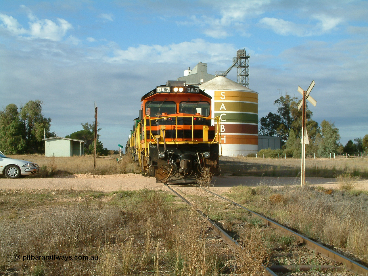 030409 080822
Warramboo, empty grain prepares to get underway following a crew change. Rebuild unit DA 7 in Australian Southern orange and black livery leads a pair of AE Goodwin built ALCo model DL531 830 class units 872 and 871, the relieved crew in the car with the long disused station building on the left and the SACBH concrete silo complex on the right rounding out the scene.
Keywords: DA-class;DA7;83713;Port-Augusta-WS;ALCo;DL531G/1;48-class;4813;rebuild;