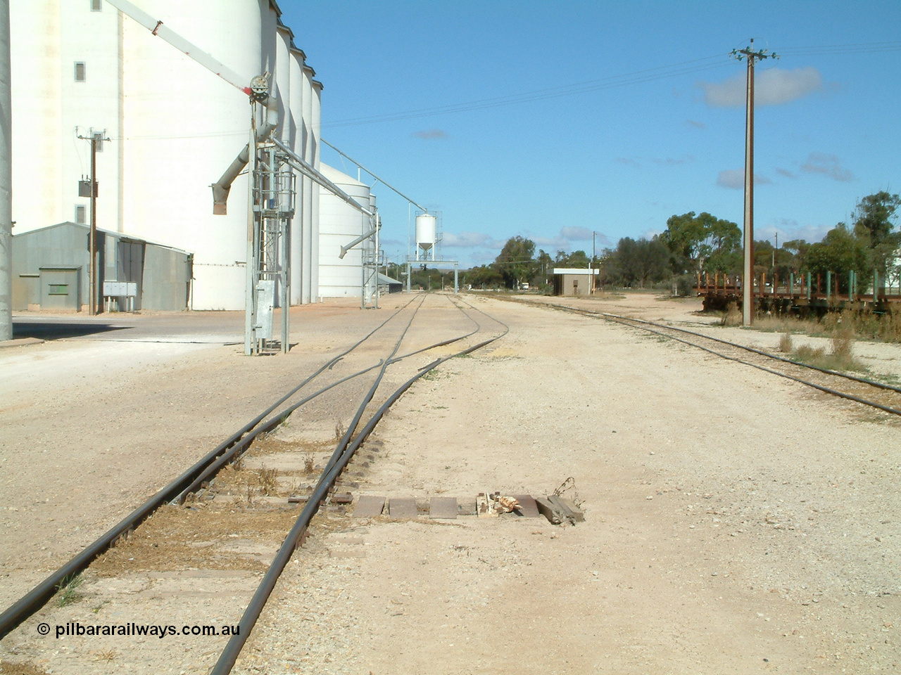 030411 110106
Kimba, station yard view looking south, point level is covered to allow road vehicles to travel over it as a tractor is sometimes used for shunting. The loadout spouts are evident along with the Ascom loadout silo and horizontal bunker beyond that.
