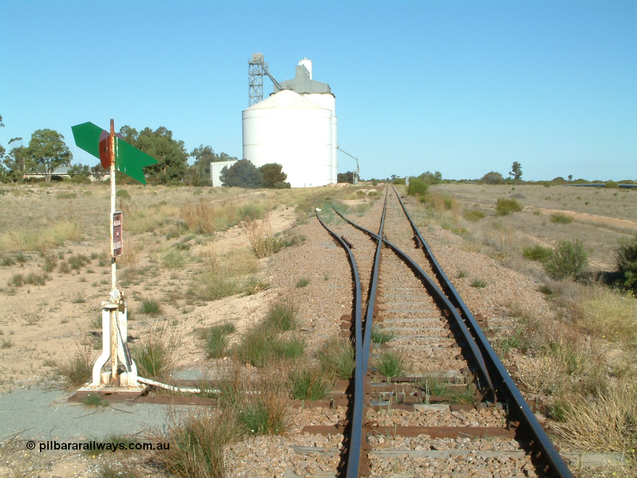 030411 160238
Cungena, 306.7 km, yard overview looking south from Thevenard end, Ascom style silo complex block 2 with concrete block 1 behind it. Station shelter visible behind tree.

