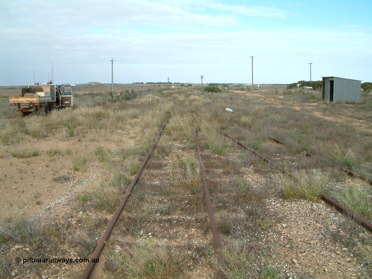 030414 154350
Penong, 505.6 km looking east with the goods loop coming in on the right to join the mainline. The car is on the grain loop. Station shelter on the right is where the original barracks were located.
