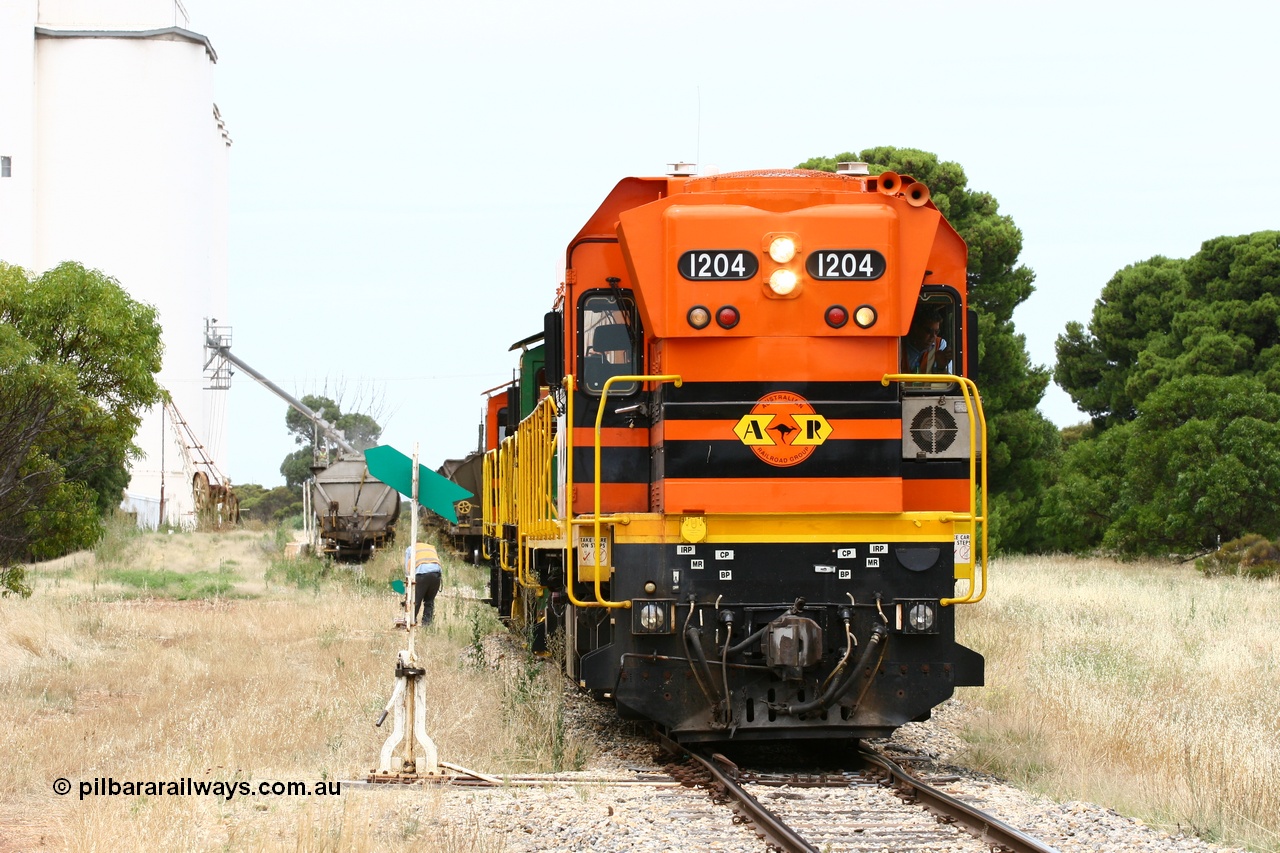 060110 2205
Yeelanna, ARG 1200 class unit 1204, a Clyde Engineering EMD model G12C serial 65-428, originally built for the WAGR as the final unit of fourteen A class locomotives in 1965 and sent to the Eyre Peninsula in July 2004 stands on the mainline as the second person restores the point for the main, a rake of waggons in grain siding await loading, with the 5 ton crane also visible. [url=https://goo.gl/maps/1JetzWBTGAw]Approx. location of image[/url].
Keywords: 1200-class;1204;Clyde-Engineering-Granville-NSW;EMD;G12C;65-428;A-class;A1514;