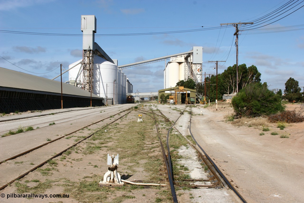 060113 2459
Thevenard, yard view looking west from No. 13 points at the front of the maintenance 'yard' with the disused grain bunker and 6DD3 running along beside the silos as it unloads at GRA, further silos form the background with the maintenance centre with stand-by loco 871 on hand and a couple of ENH hopper waggons. 13th January 2006.
