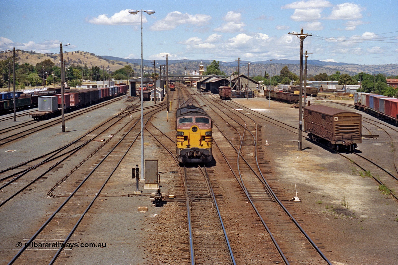 100-13
Albury station yard overview looking south from Wilson Street footbridge, NSWSRA standard gauge 44 class 4479 AE Goodwin ALCo model DL500B serial G3421-19 readies for Inter-Capital Daylight banker duty, 2 lever ground frame and point rodding, loco shops, station building and goods sheds visible, broad gauge tracks at far right with container waggons. [url=https://goo.gl/maps/nngpTA37VQekQpCt7]Geodata[/url].
Keywords: 44-class;4479;AE-Goodwin;ALCo;DL500B;G3421-19;