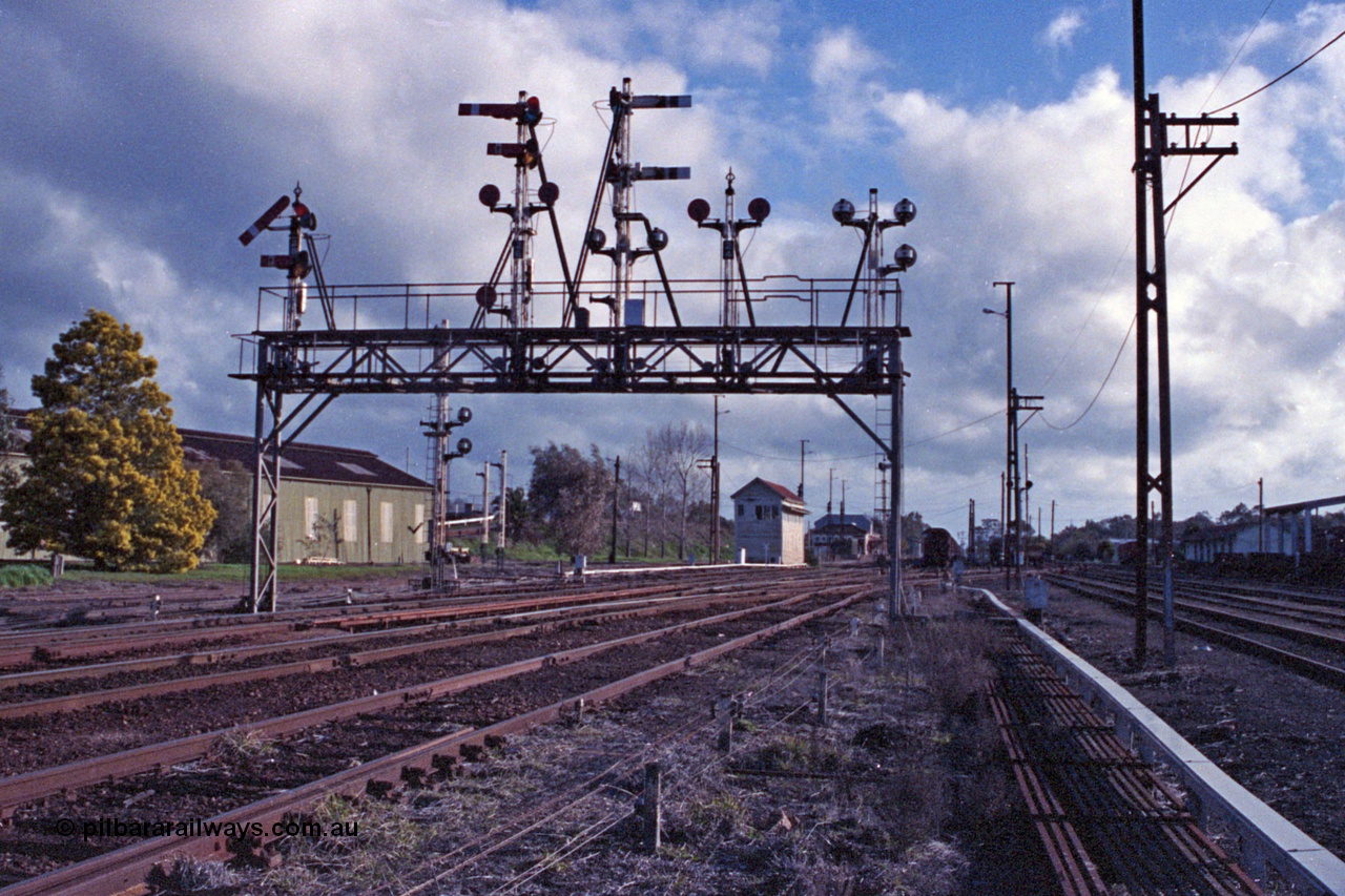 103-23
Benalla station yard overview, signal gantry still complete and intact, semaphore signal post 28 pulled off for up Albury pass, looking south, before rationalisation, workshops at left, Benalla B signal box, point rodding and signal wires, Freightgate canopy at right.
