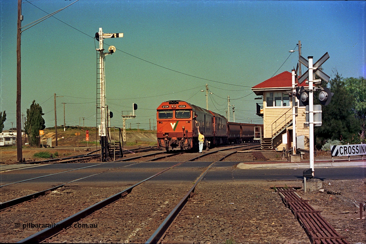 112-17
North Geelong C Box, Separation Street grade crossing, V/Line broad gauge grain train departing North Geelong Yard behind G classes G 534 Clyde Engineering EMD model JT26C-2SS serial 88-1264 and sister unit, signaller handing up electric staff for section to Gheringhap, ground dwarf signal 18 pulled off for departure, semaphores and searchlight signal posts, grade crossing, point rodding and signal box, safeworking.
Keywords: G-class;G534;Clyde-Engineering-Somerton-Victoria;EMD;JT26C-2SS;88-1264;