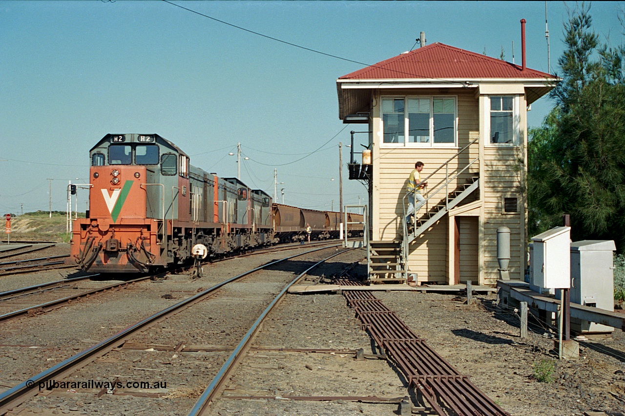 112-32
North Geelong C Box, V/Line broad gauge H class locos H 2 Clyde Engineering EMD model G18B serial 68-630, H 5 serial 68-632 and H 4 serial 68-633 shunt an empty grain train back into North Geelong yard past C Box, shunter in background, signaller returning to box, point rodding, ground dwarf signal.
Keywords: H-class;H2;Clyde-Engineering-Granville-NSW;EMD;G18B;68-630;H5;68-632;H4;68-633;