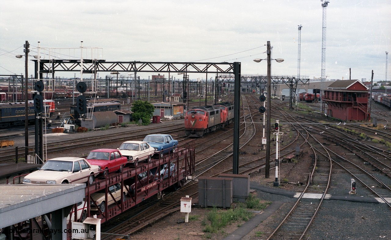 116-06
Spencer Street Station, view looking west from flyover, V/Line broad gauge A class light engines A 81 and A 62 run towards platform No.3, 'The Overland' Motorail waggons on platform No.2, DERMs 55 RM and 54 RM at left, West Tower in the middle background, Spencer Street No.1 Signal Box at right with broad gauge passenger stabling and maintenance sidings behind it, track work, points, searchlight signals and gantries and shunting signals.
