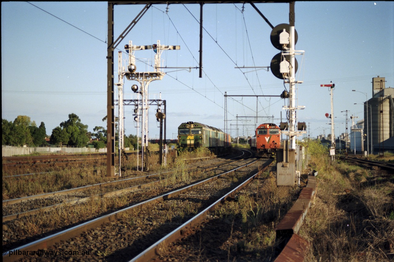 124-17
Sunshine looking from the passenger lines across to the Independent Through Goods lines, signal post 71 at camera, disc and semaphore signal posts 31 and 31B for control of the Independent Trough Goods lines, down Adelaide broad gauge goods train waiting to cross over the passenger lines, BL classes Clyde Engineering EMD model JT26C-2SS serial 83-1014 and BL 35 Clyde Engineering EMD model JT26C-2SS serial 83-1019 in AN livery, standard gauge Sunshine Loop to the left of train, V/Line broad gauge down passenger train with N class N 471 Clyde Engineering EMD model JT22HC-2 serial 87-1200 'City of Benalla' passing on passenger lines, Newport Loop Line and GEB sidings at far right.
Keywords: N-class;N471;Clyde-Engineering-Somerton-Victoria;EMD;JT22HC-2;87-1200;